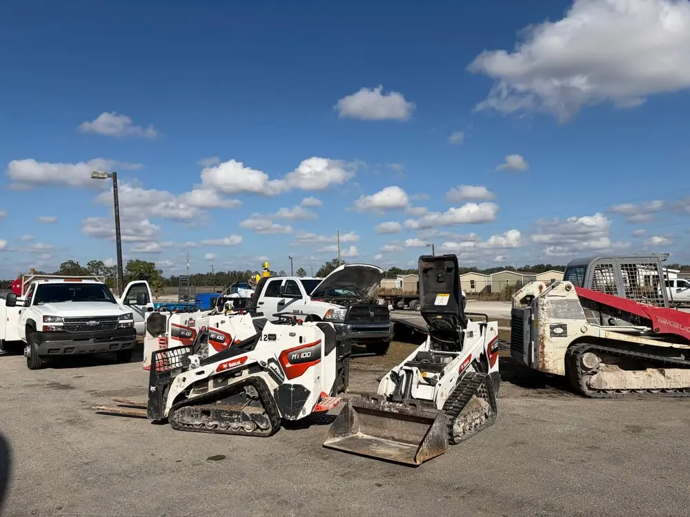 Bobcat mini track loaders and service trucks lined up in a contractor yard