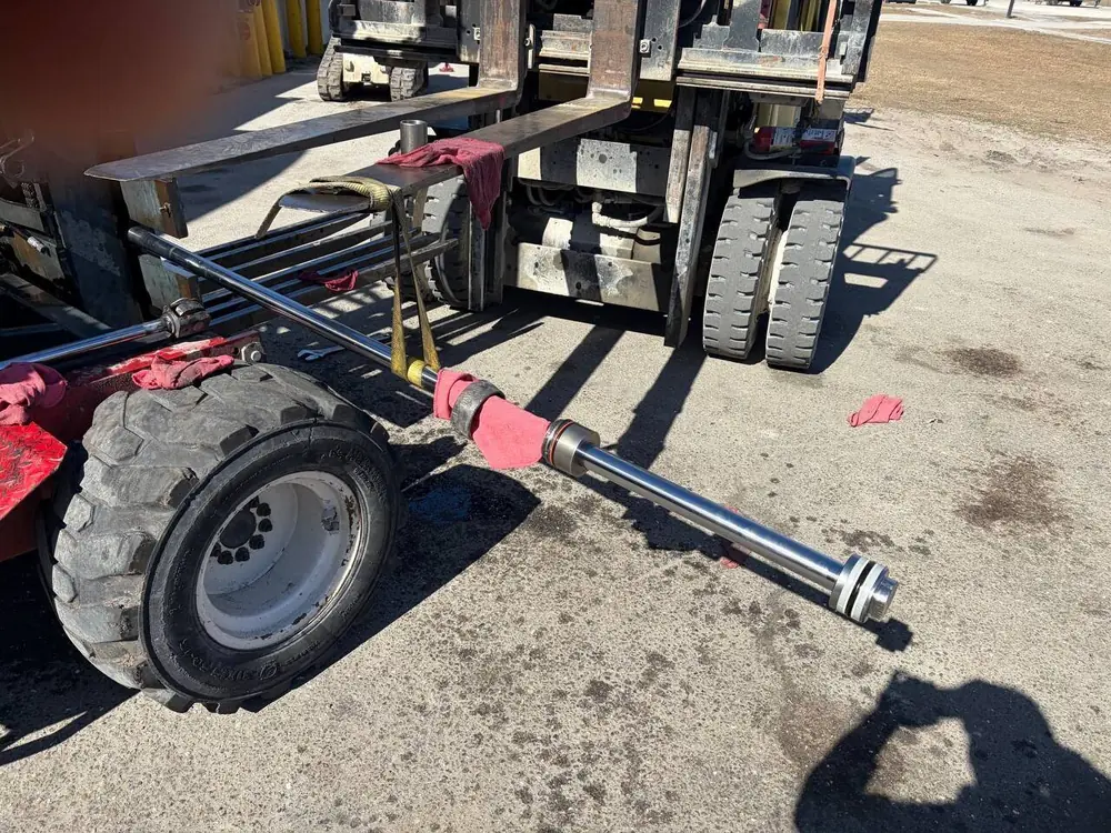 Hydraulic cylinder removed for repair beside a rough-terrain forklift