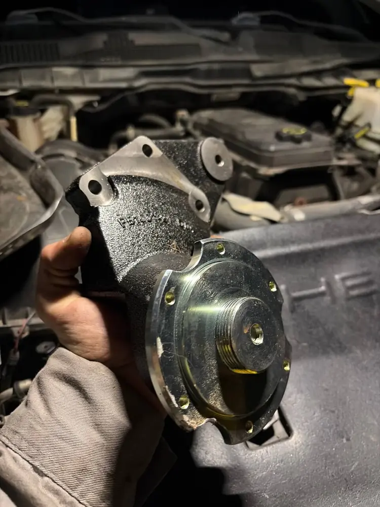 Technician holding a replacement water pump at an open engine bay during a night call